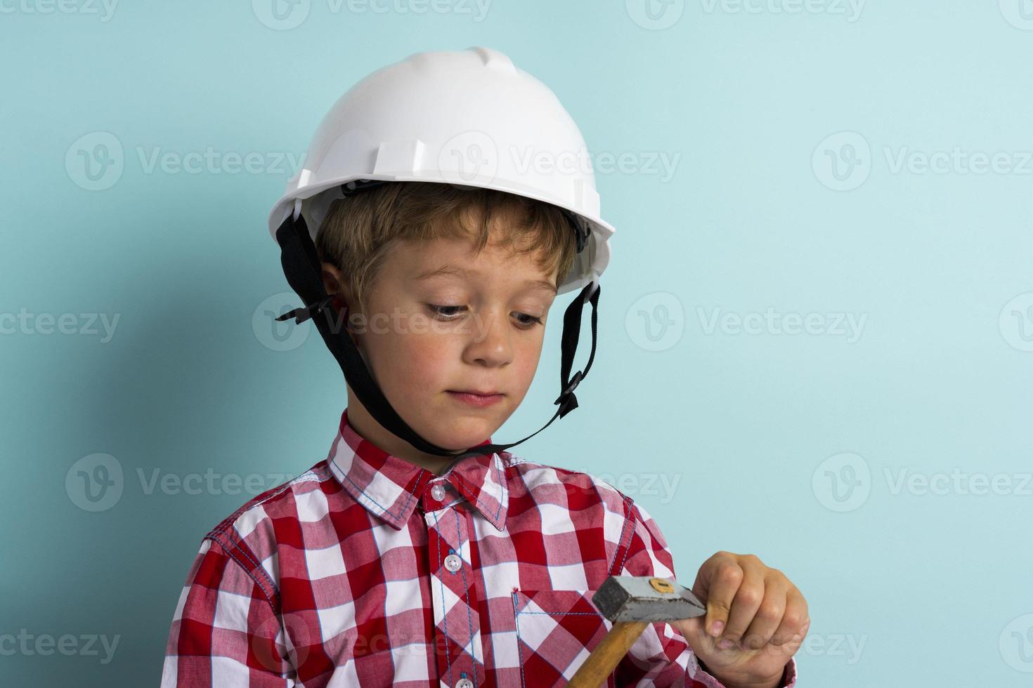 A cute boy in a plaid shirt and a construction helmet with a hammer in his hand photo