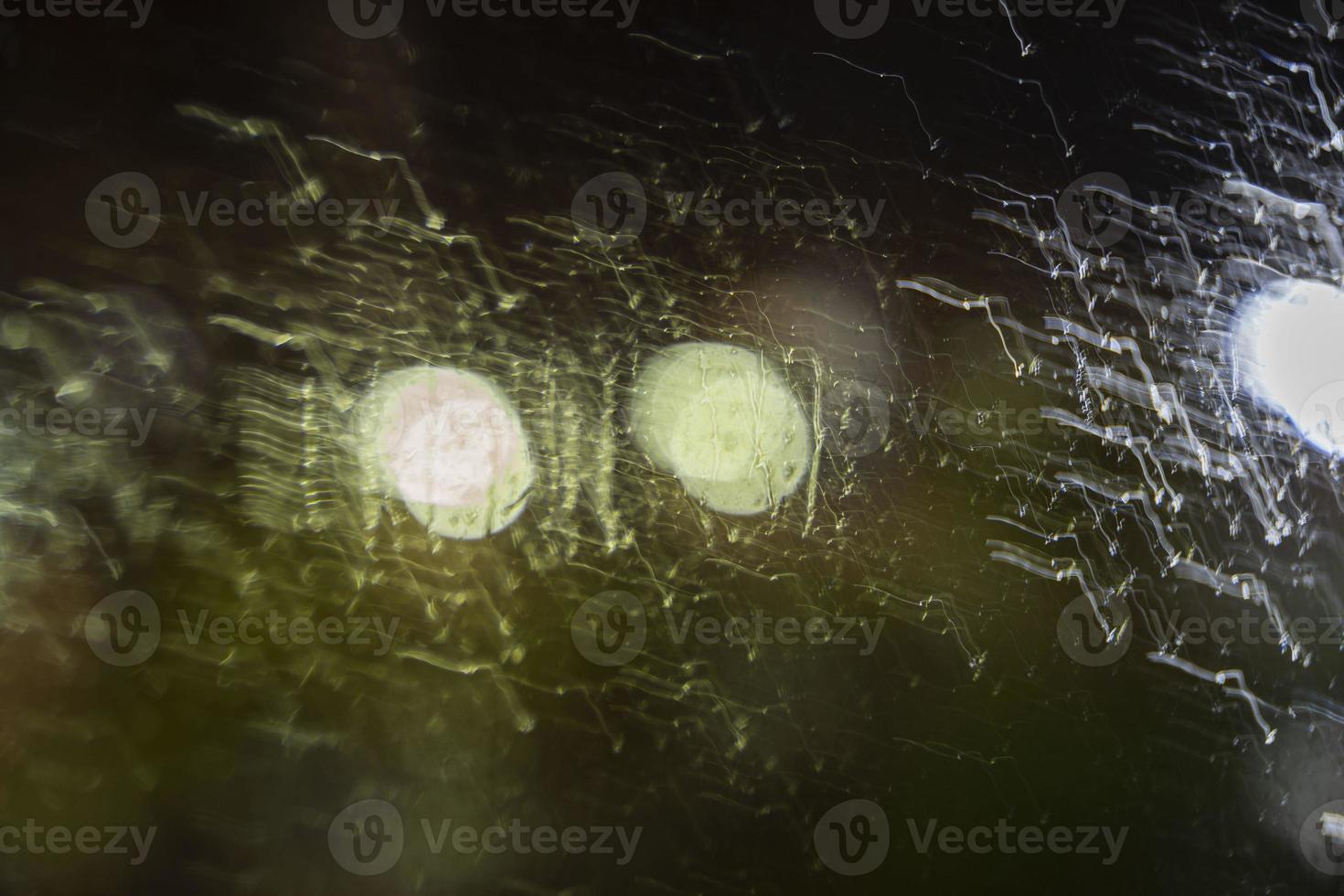 Night unfocused view through wet glass with raindrops on the background of street lights, blurred background photo
