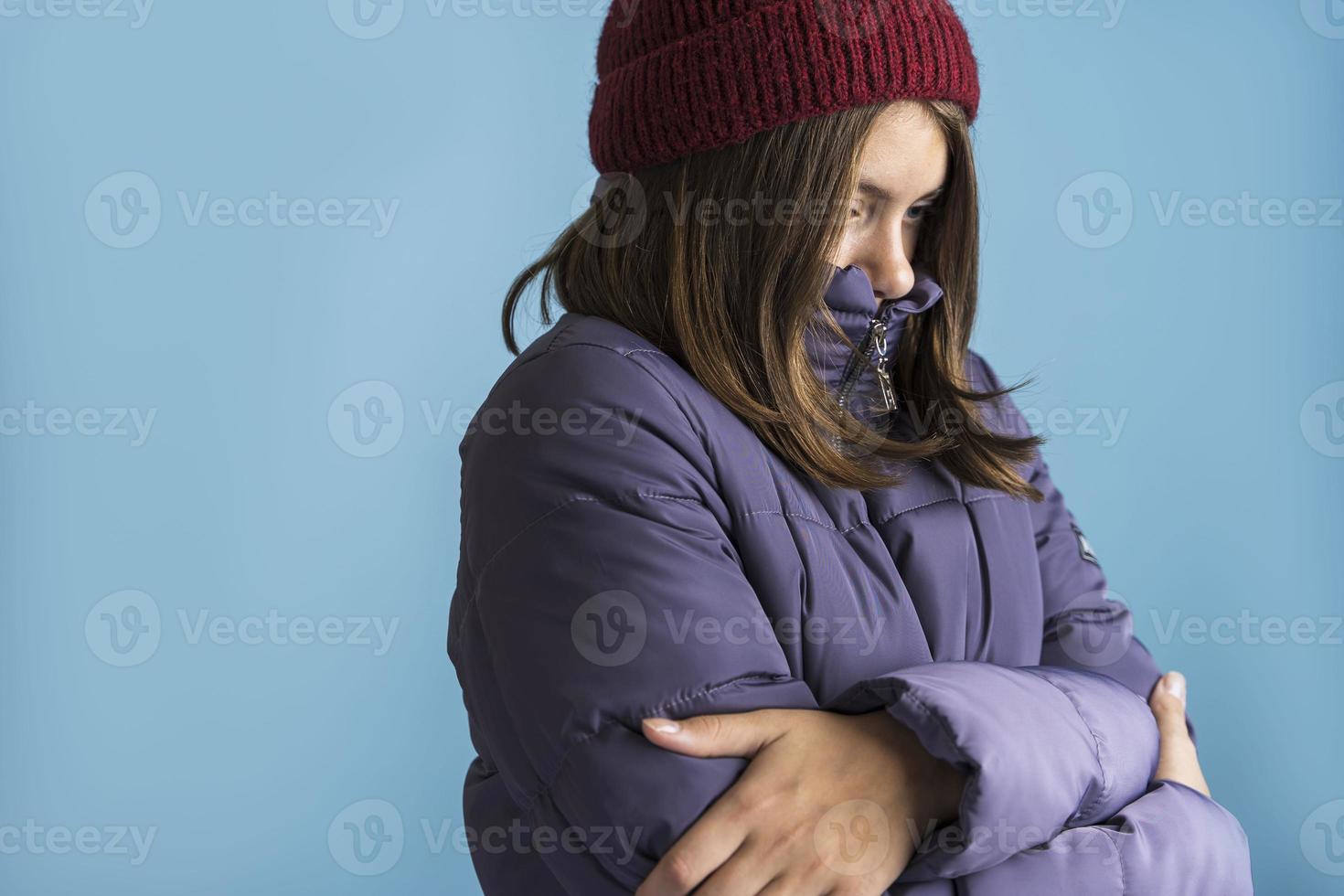una chica hermosa con un sombrero de punto y una chaqueta cálida sobre un fondo azul, la chica está congelada, una belleza congelada foto
