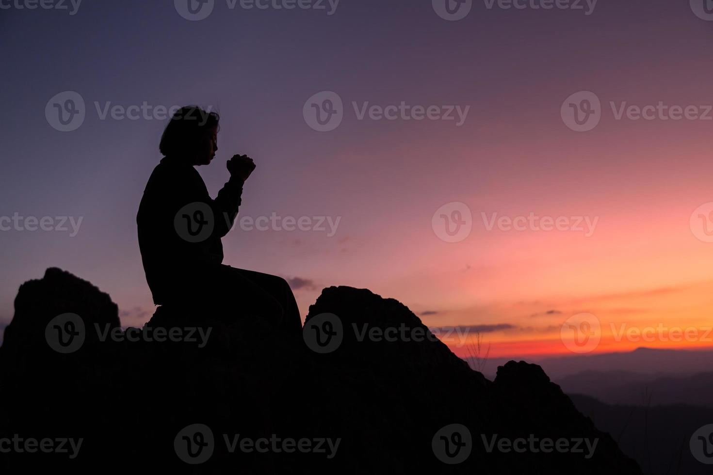 cristianismo de fe del concepto de adoración cristiana. la oración espiritual entrega el brillo del sol con un hermoso fondo de puesta de sol borroso. mujer rezando a dios con bendición esperanzadora contra la puesta de sol. foto