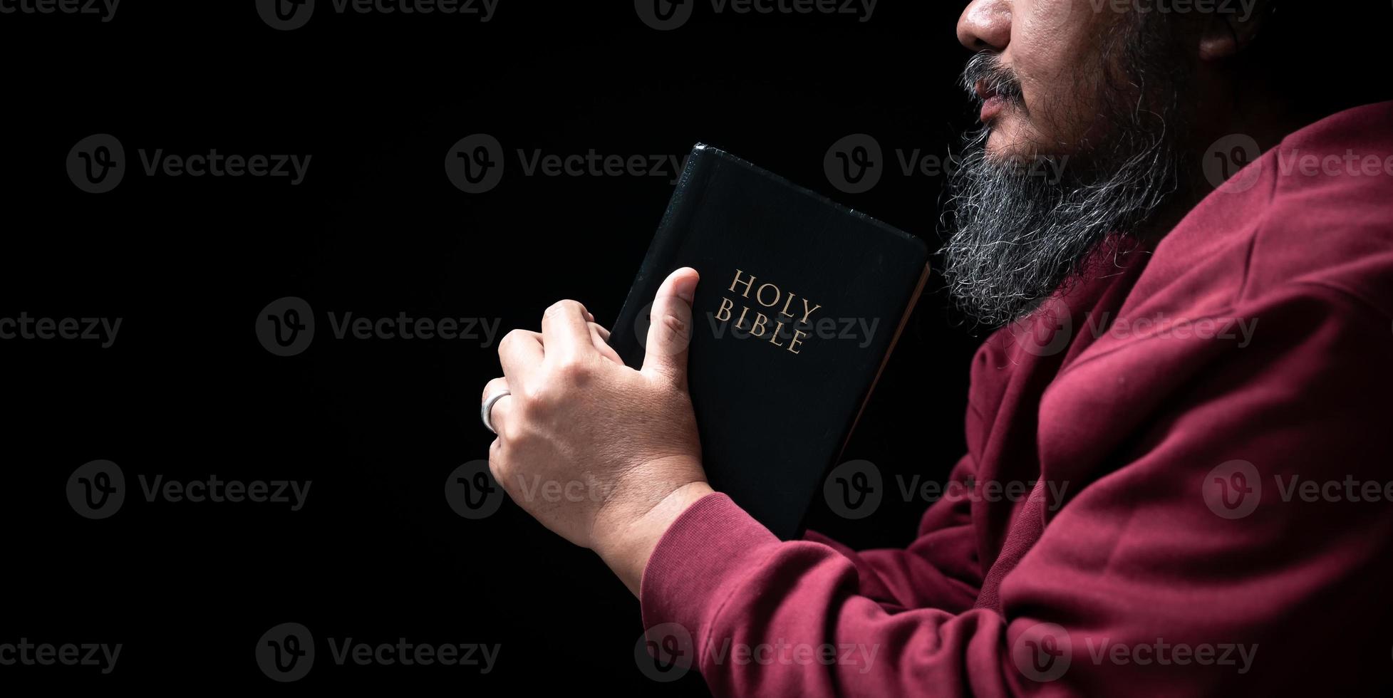 Hands folded in prayer on a Holy Bible in church concept for faith, spirituality and religion, man praying in morning. Man hand with Bible praying. Person Christian who faith in Jesus worship in dark. photo