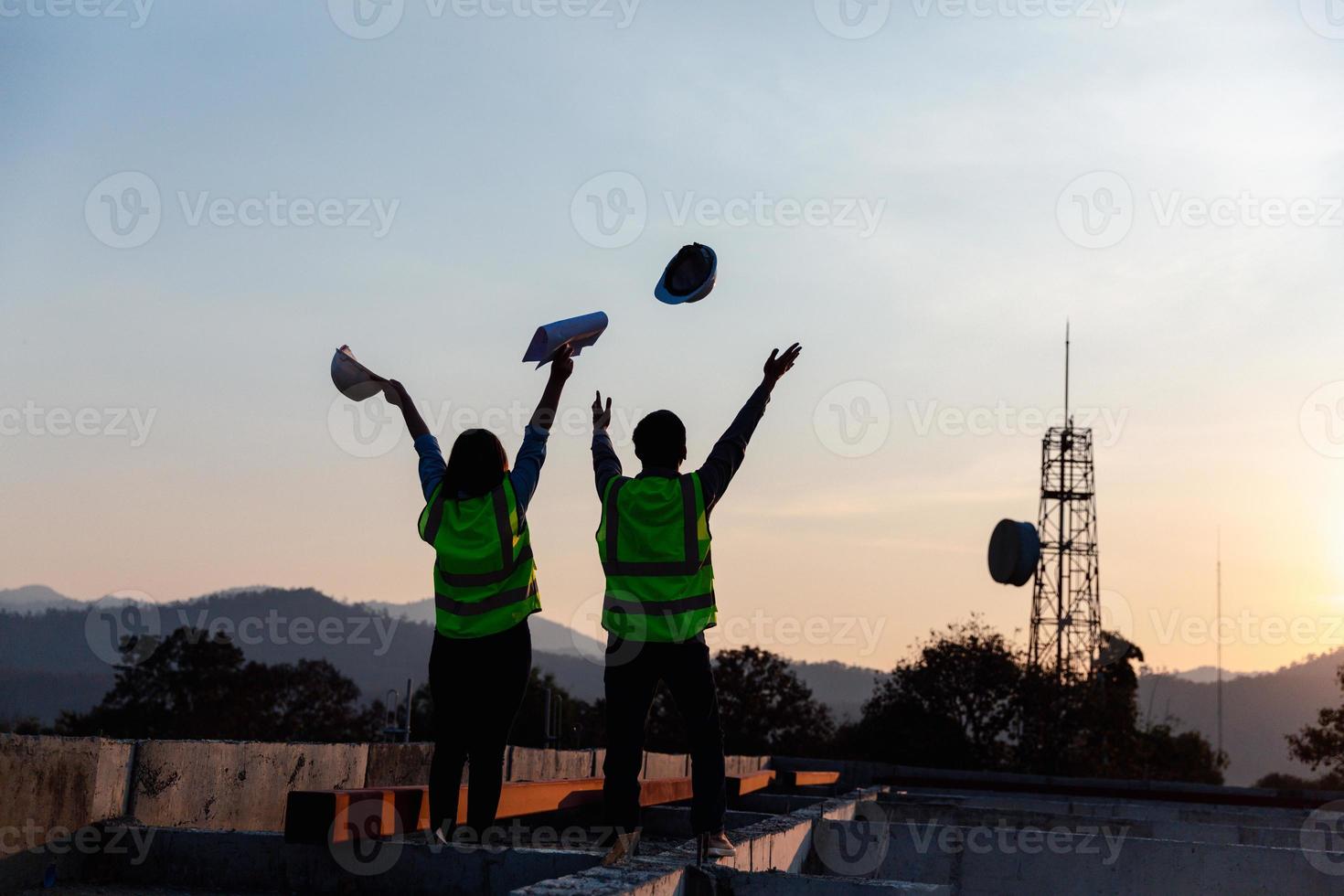 Silhouette image of engineer civil and construction worker throw up safety helmet and construction drawing against the background of surreal construction site in twilight or dark cityscape. photo