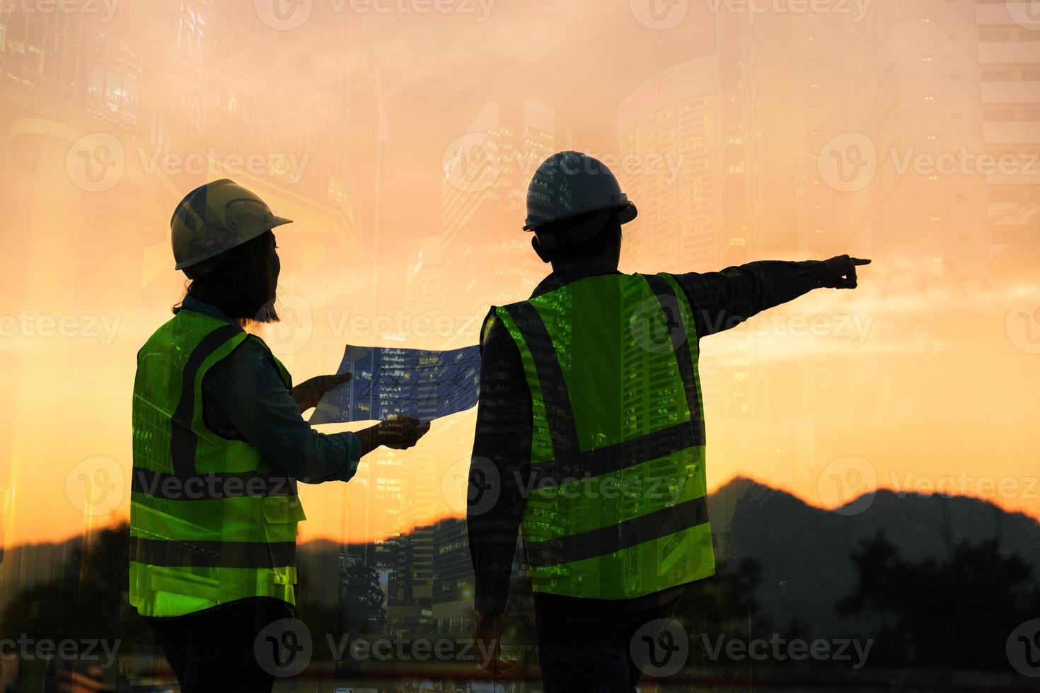 Double exposure image of engineer civil and construction worker with safety helmet and construction drawing against the background of surreal construction site in the night city or dark cityscape. photo