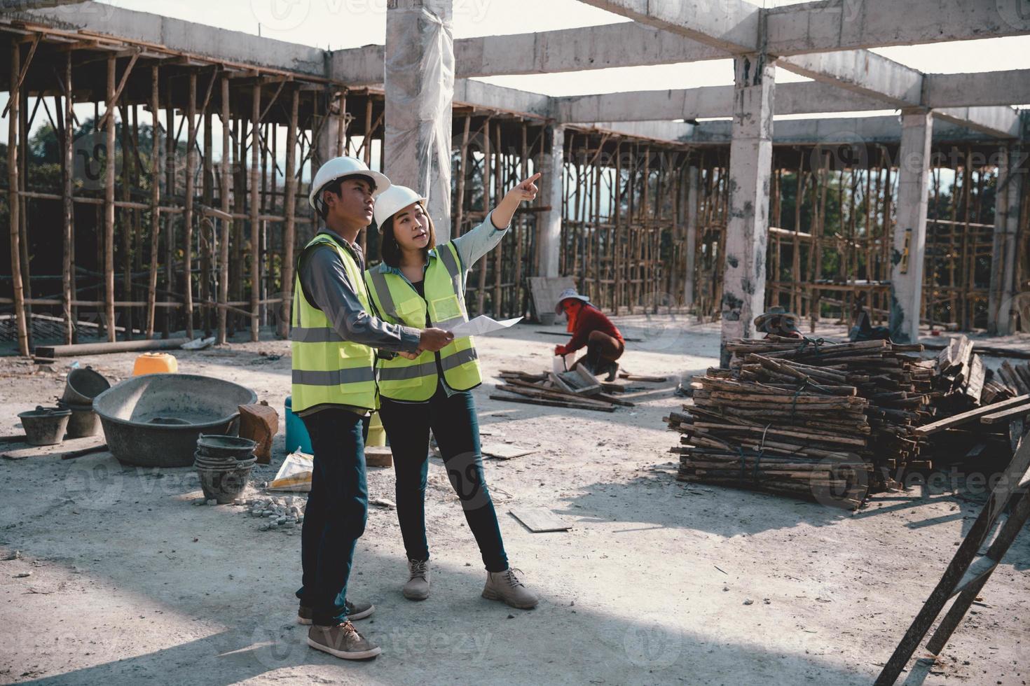 Two specialists inspect commercial, Industrial building construction site. Real estate project with civil engineer, designing commercial buildings on paper. Skyscraper concrete formwork frames. photo