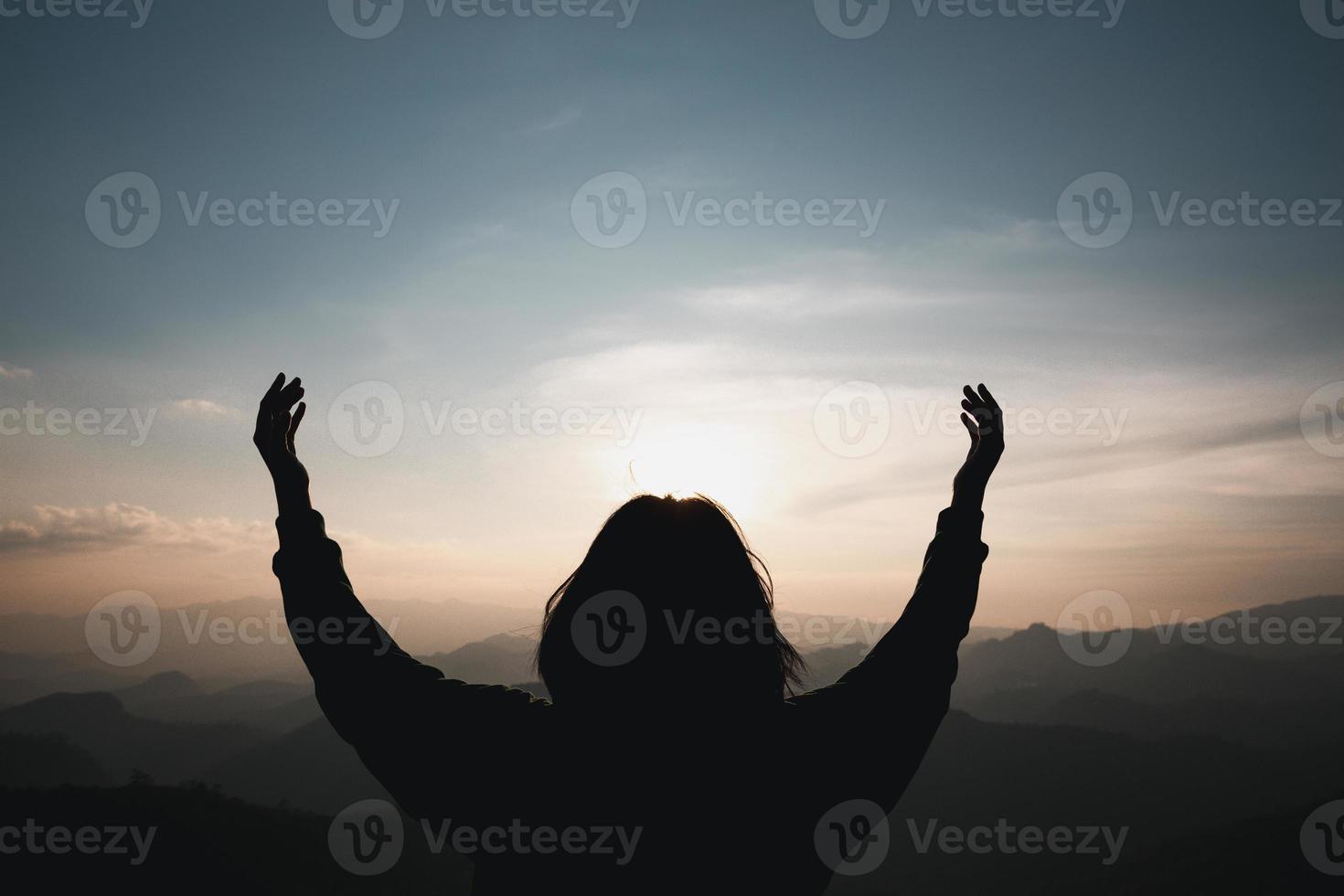 cristianismo de fe del concepto de adoración cristiana. la oración espiritual entrega el brillo del sol con un hermoso fondo de puesta de sol borroso. mujer rezando a dios con bendición esperanzadora contra la puesta de sol. foto