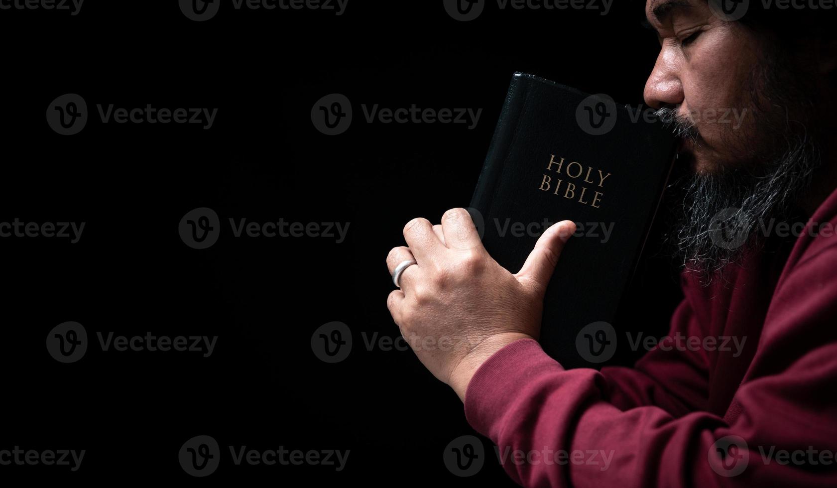 Hands folded in prayer on a Holy Bible in church concept for faith, spirituality and religion, man praying in morning. Man hand with Bible praying. Person Christian who faith in Jesus worship in dark. photo