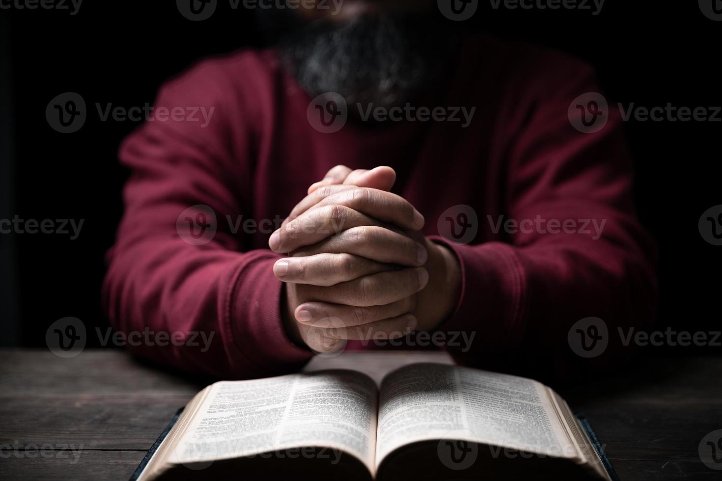 Hands folded in prayer on a Holy Bible in church concept for faith, spirituality and religion, man praying in morning. Man hand with Bible praying. Person Christian who faith in Jesus worship in dark. photo