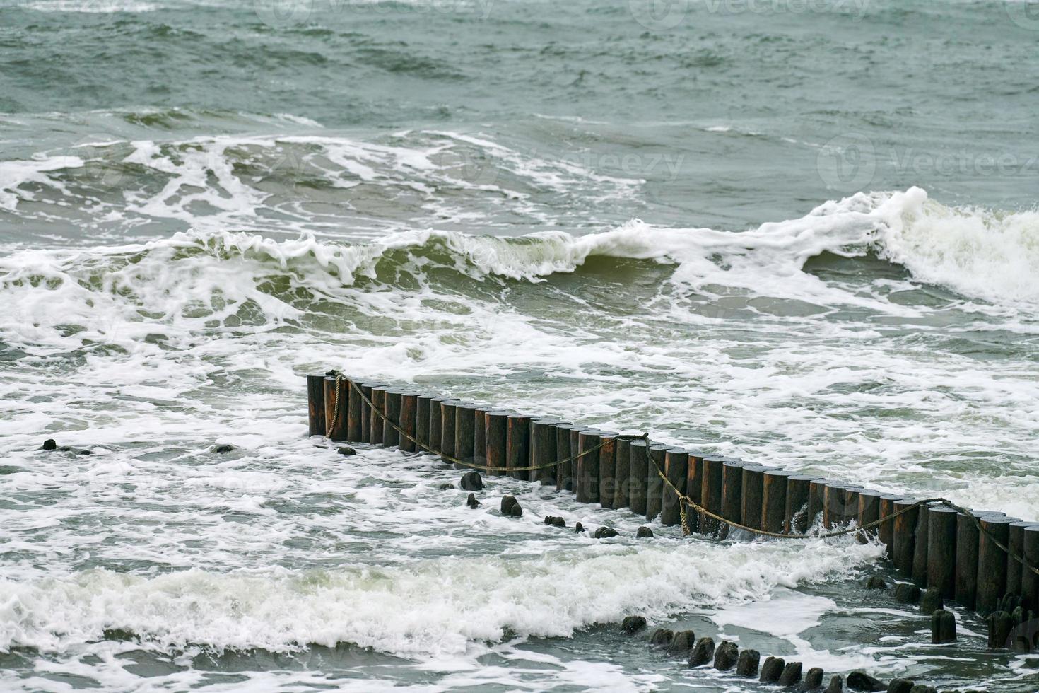 View of blue sea with foaming waves and wooden breakwaters photo