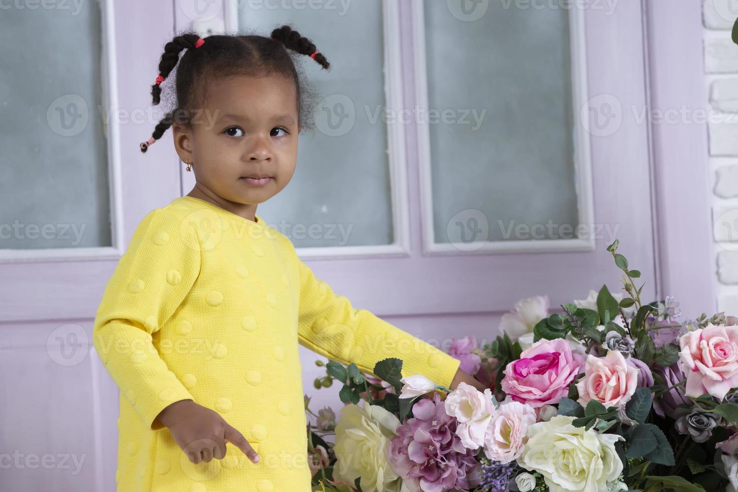Little African American girl in a yellow dress touches a bouquet of flowers with her hand. photo