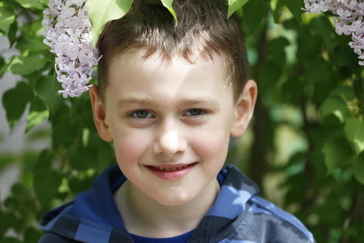 bielorrusia, ciudad de gomil, 16 de mayo de 2016. calle de la ciudad. un hermoso niño está parado junto a un arbusto de lilas y sonríe. foto