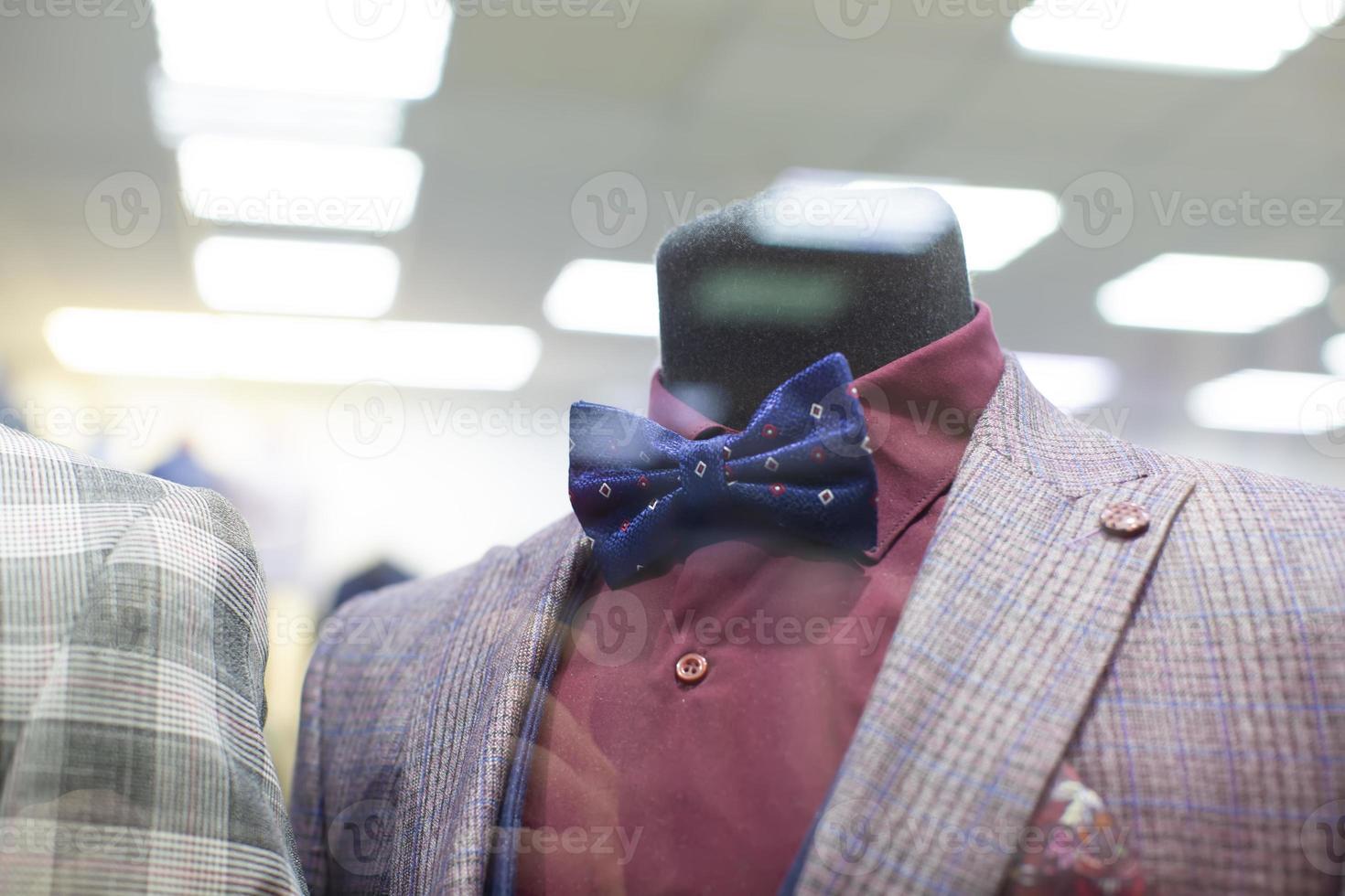 In the shop window is a mannequin in a formal suit and bow tie. photo