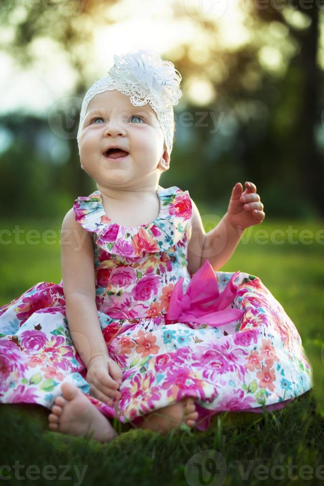 Happy little girl sits on the grass and laughs. Beautiful child. Little baby up to a year old on a summer meadow. photo