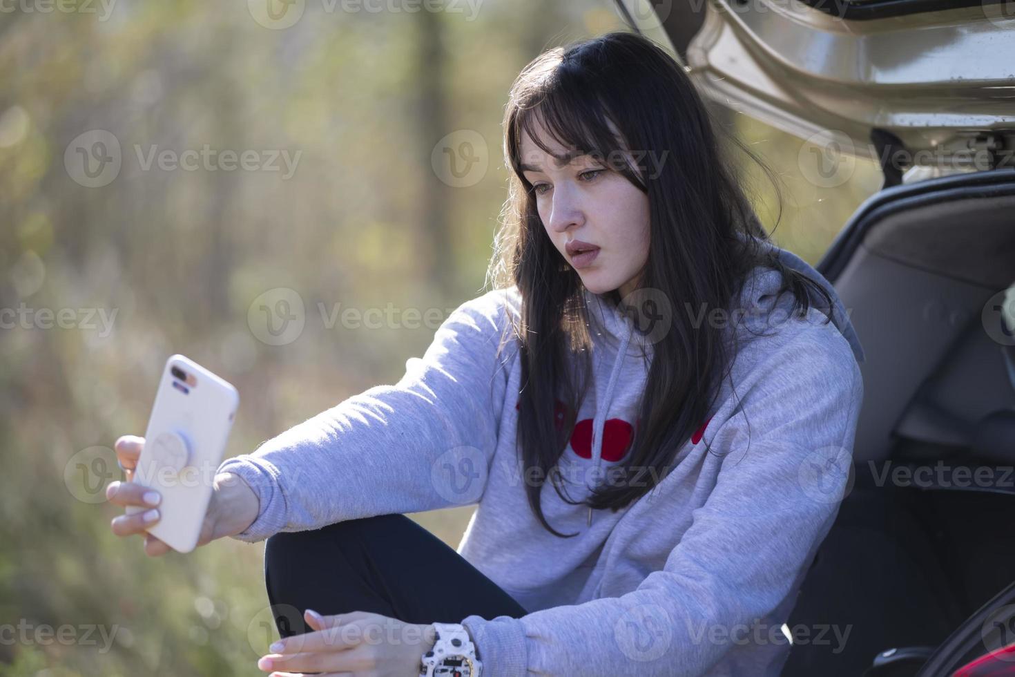 Portrait of a beautiful girl outdoors who uses a smartphone, shares digital content with each other and enjoys taking a selfie picture. photo