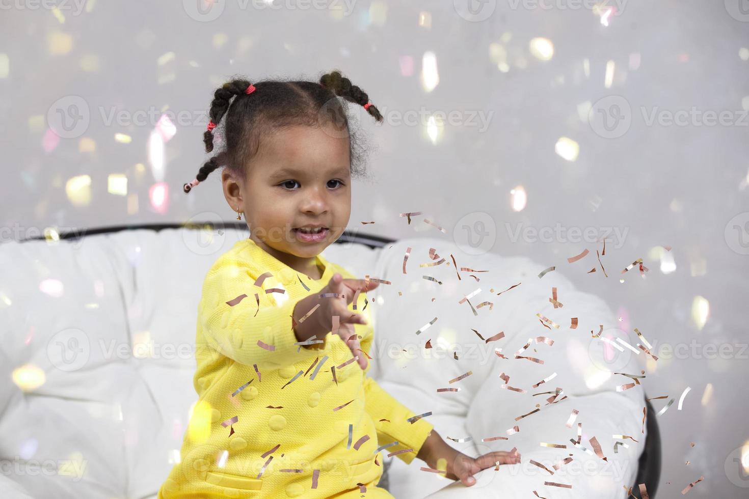 Little happy African American girl catches confetti. photo