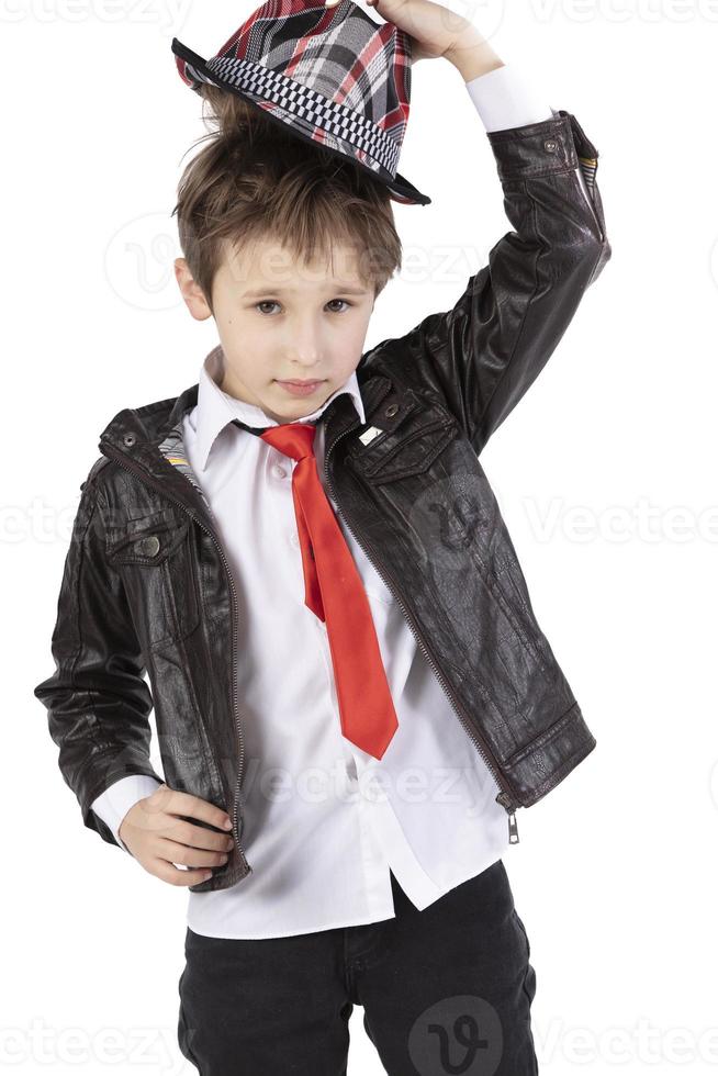 Funny little boy in a leather jacket, elegant hat and red tie. Red child on a white background. Seven year old boy. Take off your hat. photo