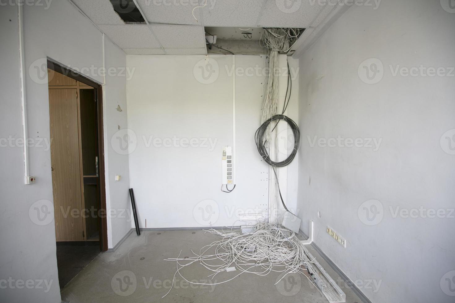 In an empty office, lots of electrical wires hang from the ceiling. photo