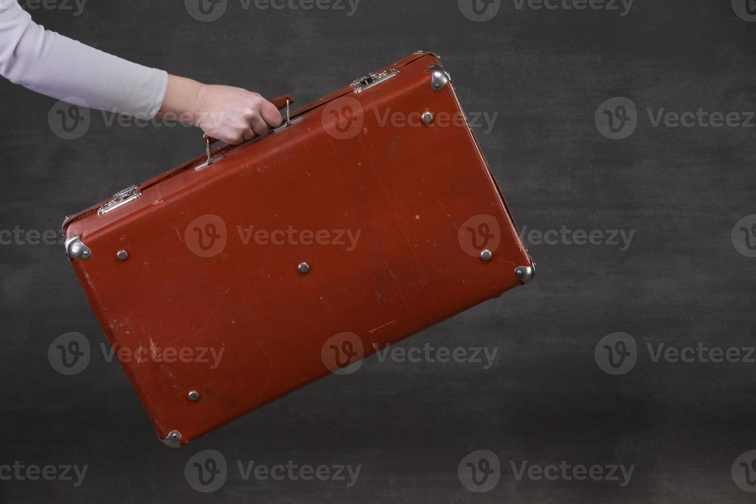 In hand is a brown retro suitcase on a gray background. photo