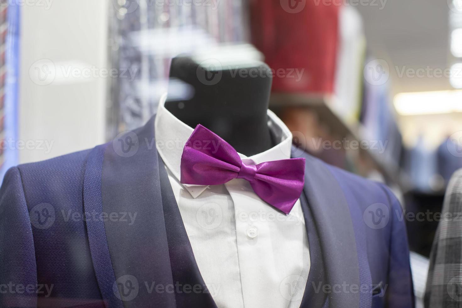 In the shop window is a mannequin in a formal suit and bow tie. photo