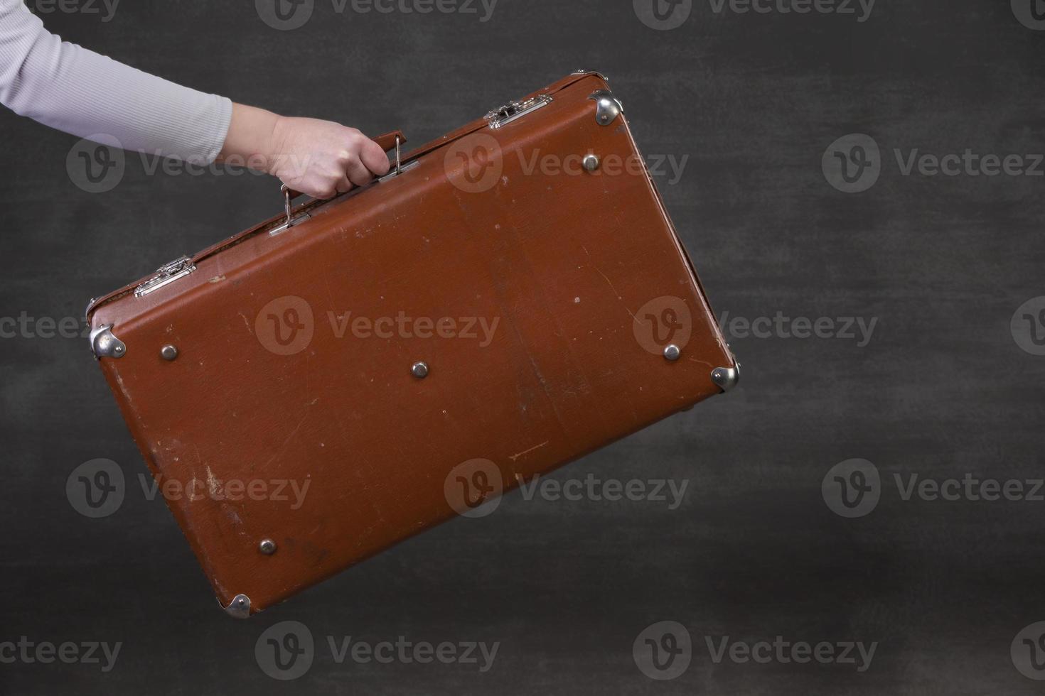 In hand is a brown retro suitcase on a gray background. photo