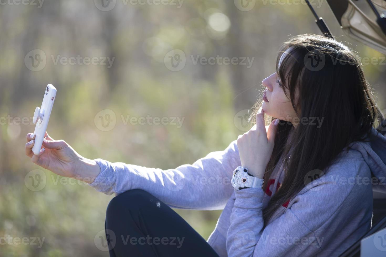 Portrait of a beautiful girl outdoors who uses a smartphone, shares digital content with each other and enjoys taking a selfie picture. photo