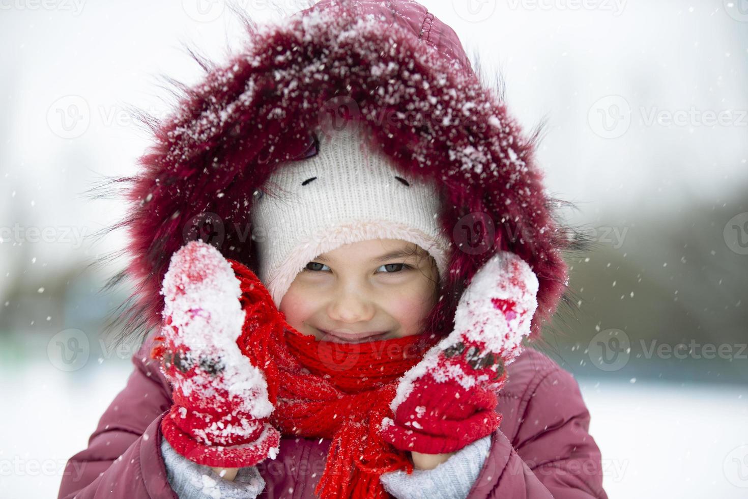 niño en invierno. una niña pequeña con un gorro y una capucha mira a la cámara y sonríe. foto