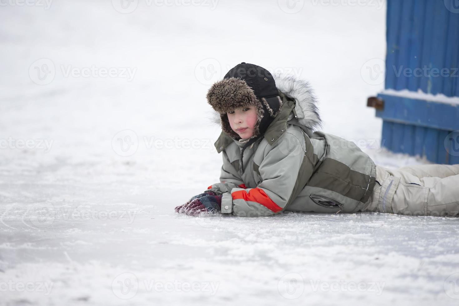 A little boy in a fur hat lies on the snow. Child in winter. photo