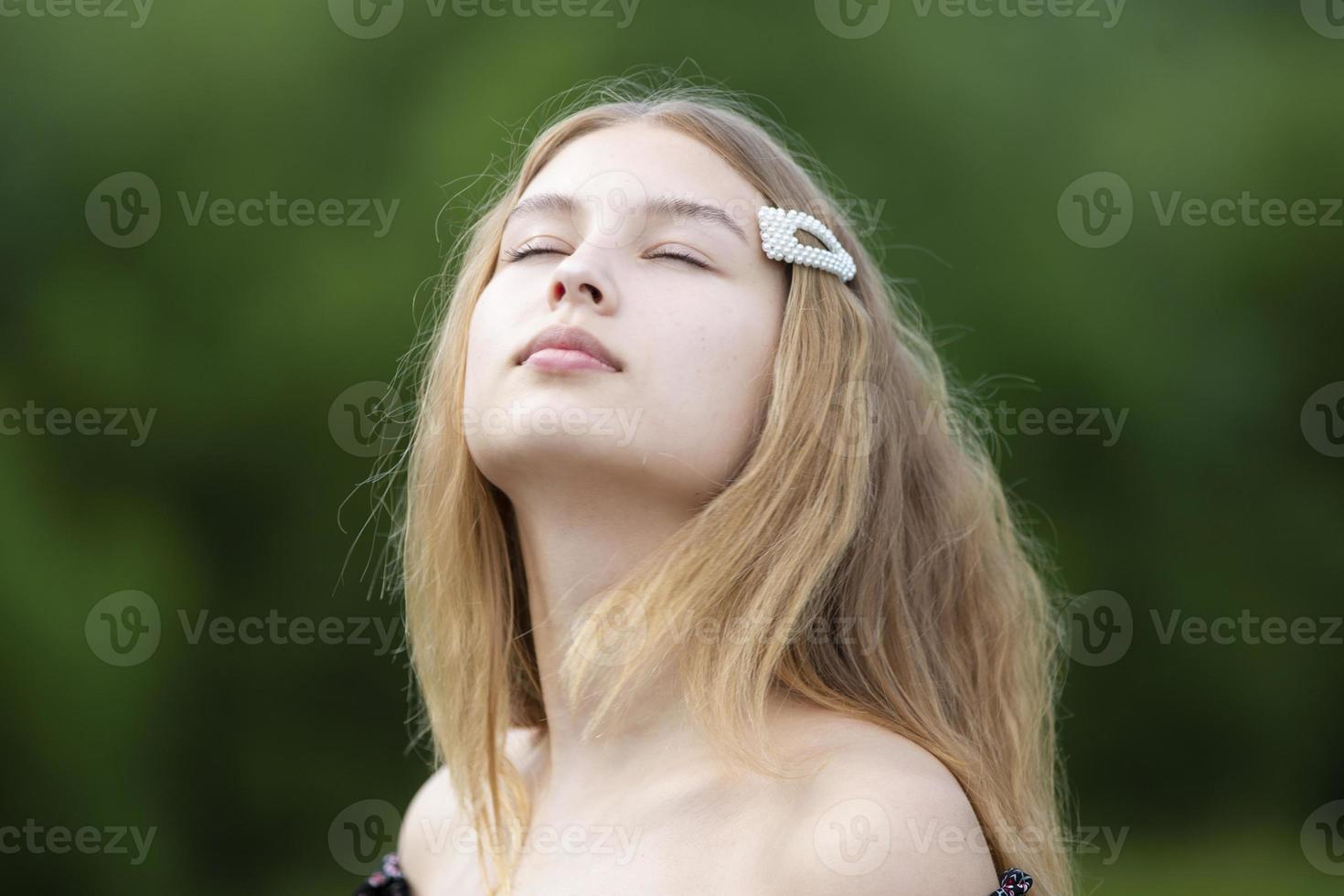 A beautiful girl with long hair closed her eyes on a summer background. The face of a fair-haired teenage girl. photo