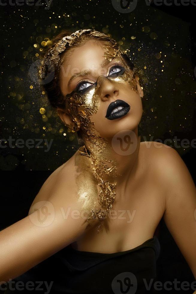 Fashion art Golden skin. Girl Model with Festive Golden Glamor Brilliant Professional Makeup. Creative makeup with golden foil. photo