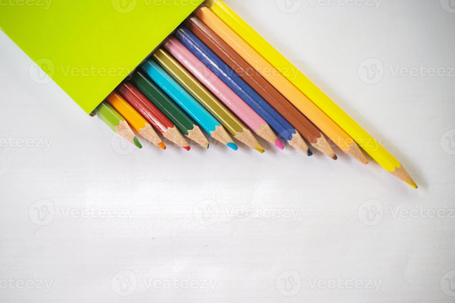 colored pencils neatly lined up on white paper, there are sharpeners and leaves photo