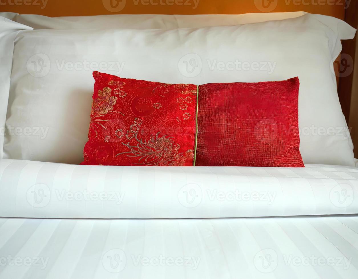 Close up A red Chinese style fabric scatter cushion, backrest pillow, placed in front of double white pillows on the hotel bed, turn down service with copy space photo