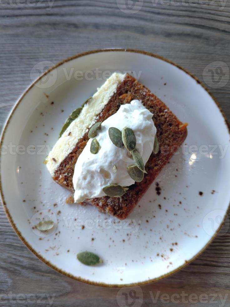 Directly above view A slice of carrot cake topping with cream sprinkle with pumpkin seeds in the white ceramic plates on wooden table, a dessert menu in Bangkok Cafe photo