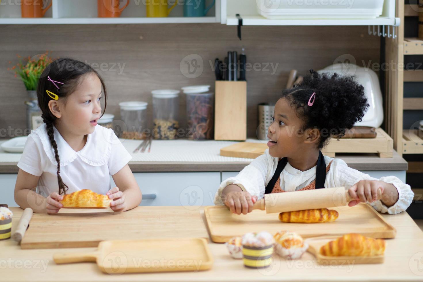 dos niños pequeños felices cocinando juntos, sacando masa, parados en una encimera de madera en una cocina moderna, lindos caseros foto