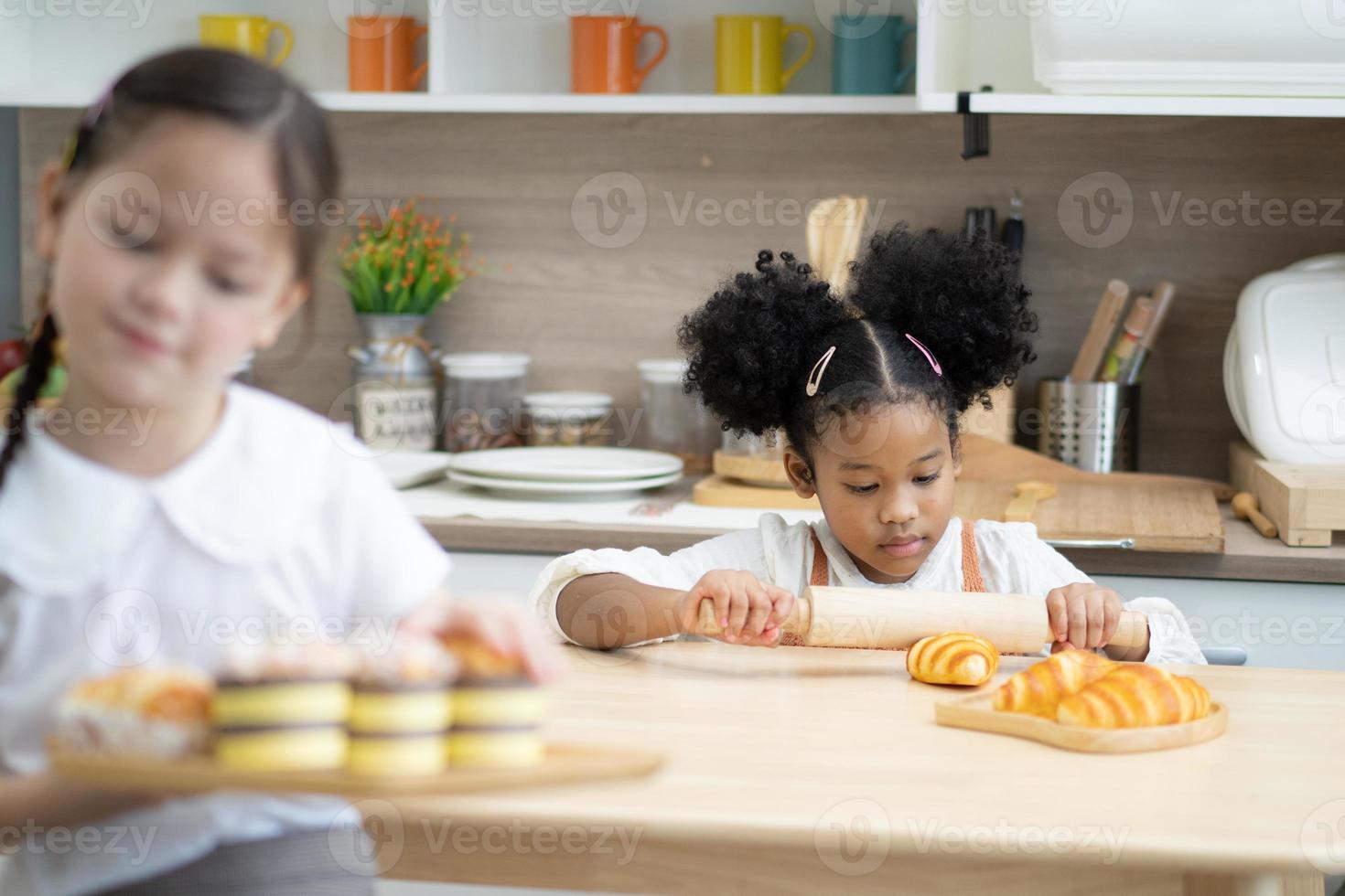 dos niños pequeños felices cocinando juntos, sacando masa, parados en una encimera de madera en una cocina moderna, lindos caseros foto