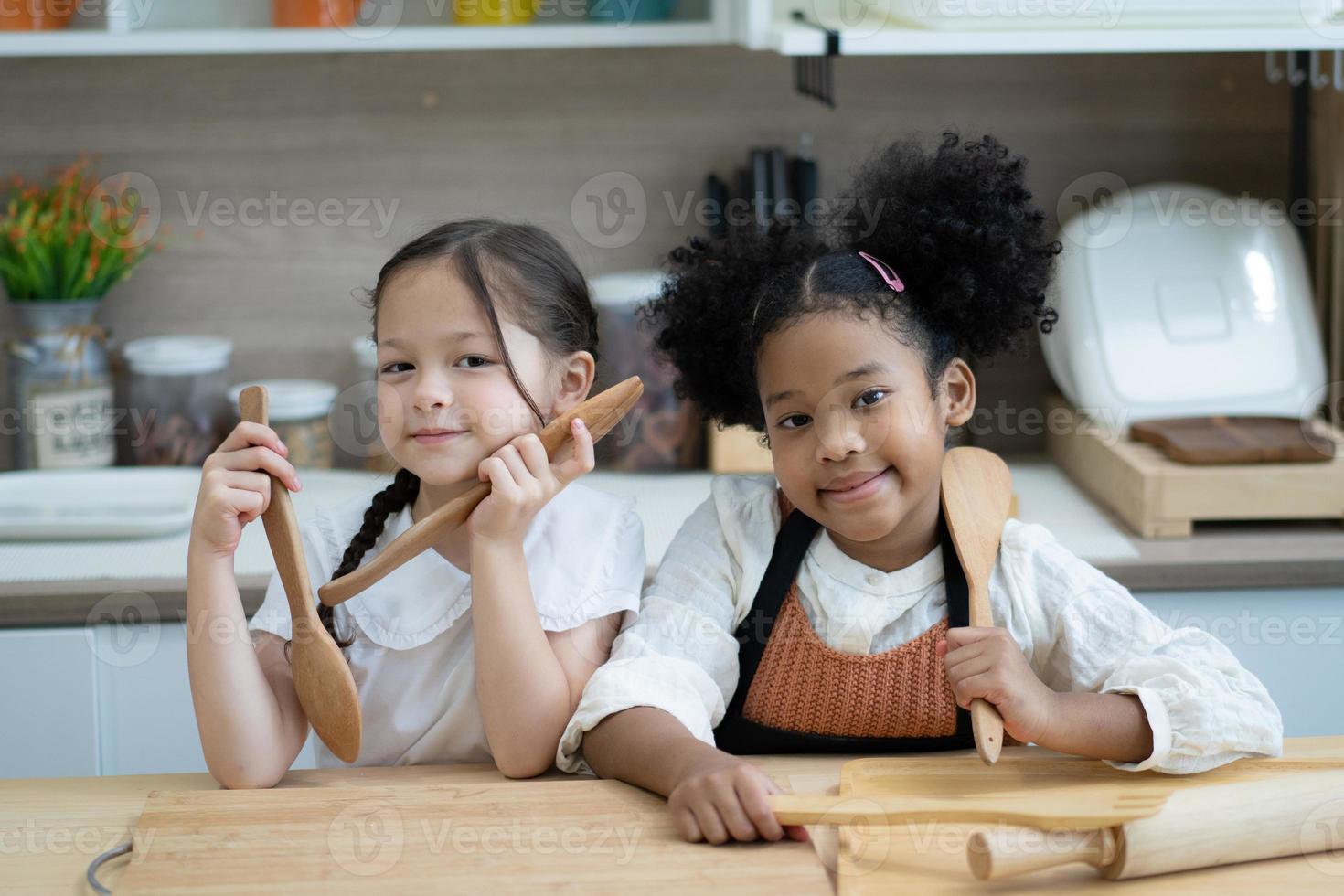 Two happy little kids siblings cooking together, rolling out dough, standing at wooden countertop in modern kitchen, cute homemade photo