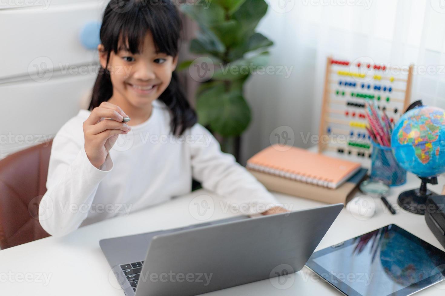 colegiala asiática haciendo su tarea con una laptop en casa. los niños usan aparatos para estudiar. educación y aprendizaje a distancia para niños. educación en el hogar durante la cuarentena. Quédate en casa foto