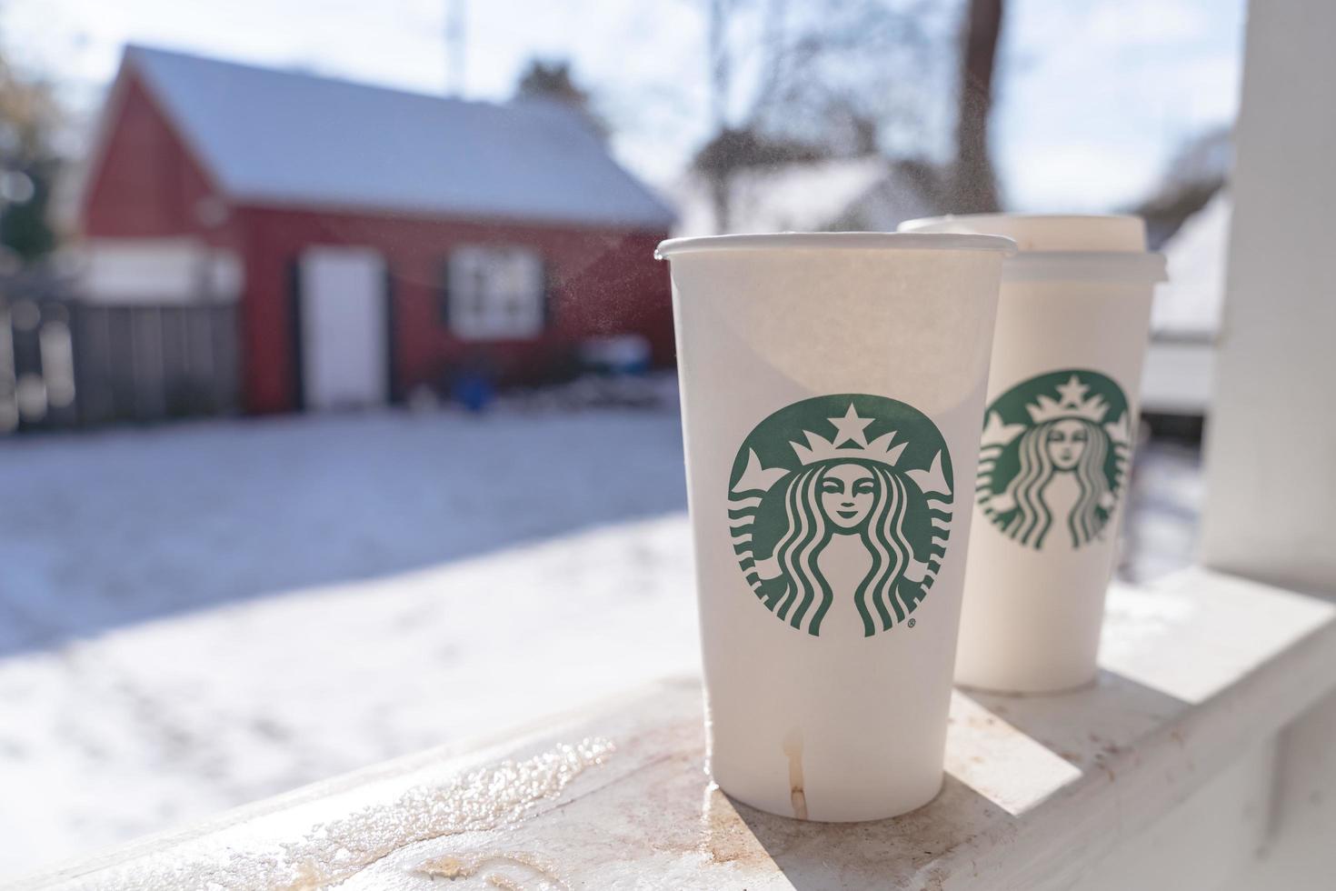 Marinette,WI,USA - Nov14, 2023- Cups of Starbucks Hot Coffee put on white snow in winter garden, fresh and hot beverage take away concept.Starbucks Cafe Coffee Shop. photo