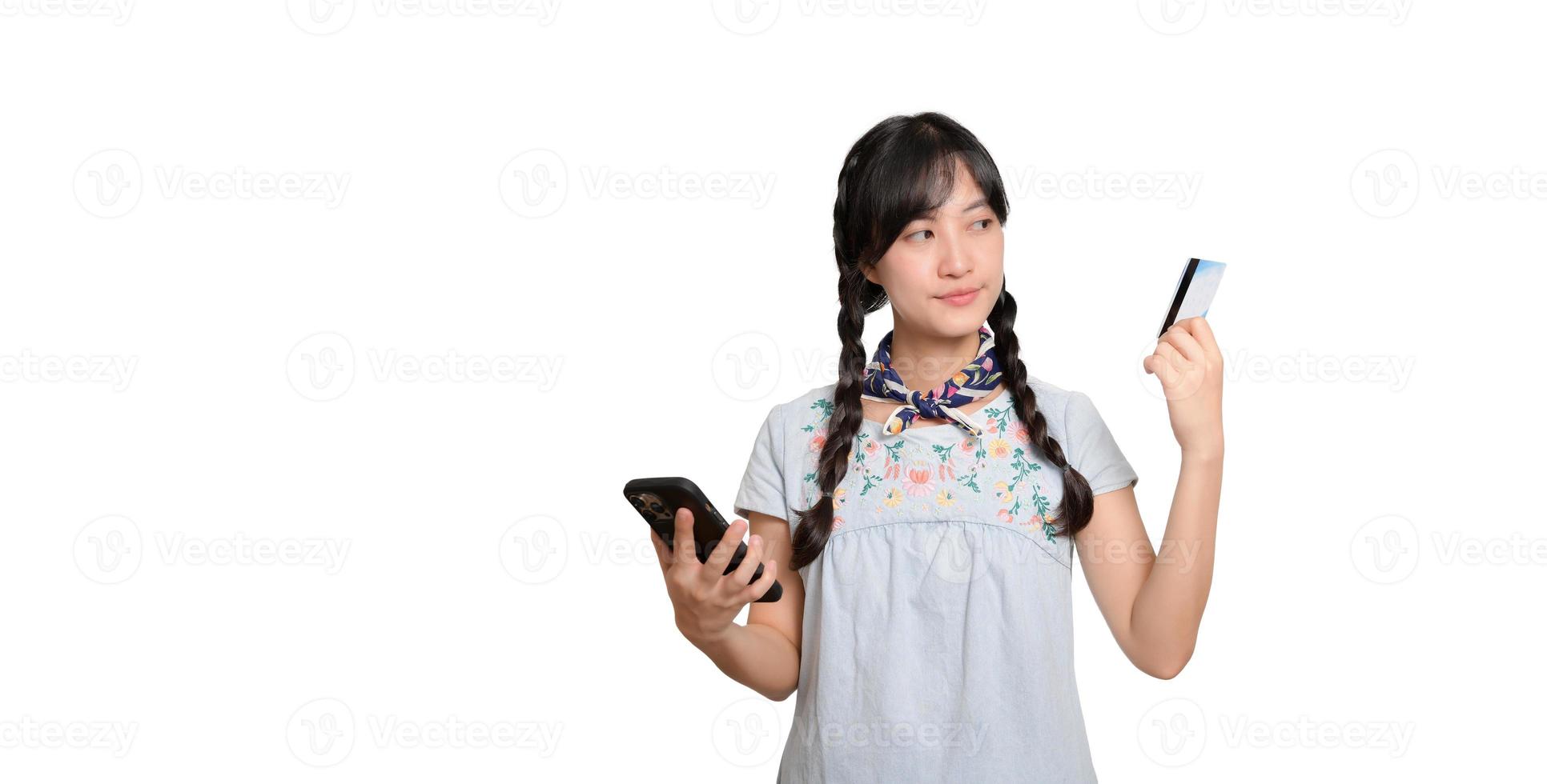 Portrait of beautiful happy young asian woman in denim dress holding credit card and smartphone on white background. studio shot photo