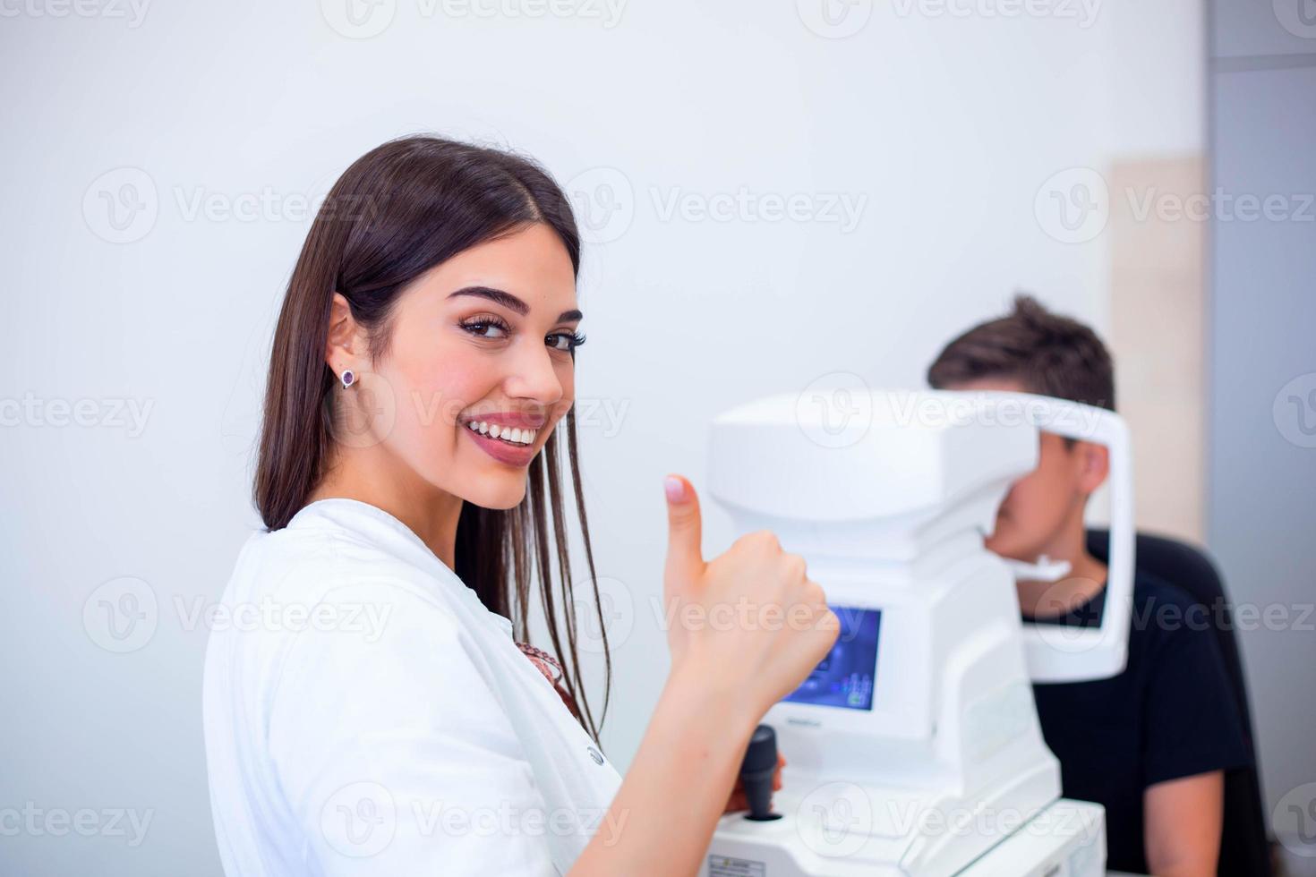 Female oculist using machine for checking eye sight in clinic. Little boy looking at equipment and doctor testing eye pupil in optical store. Concept of eye care and health. photo