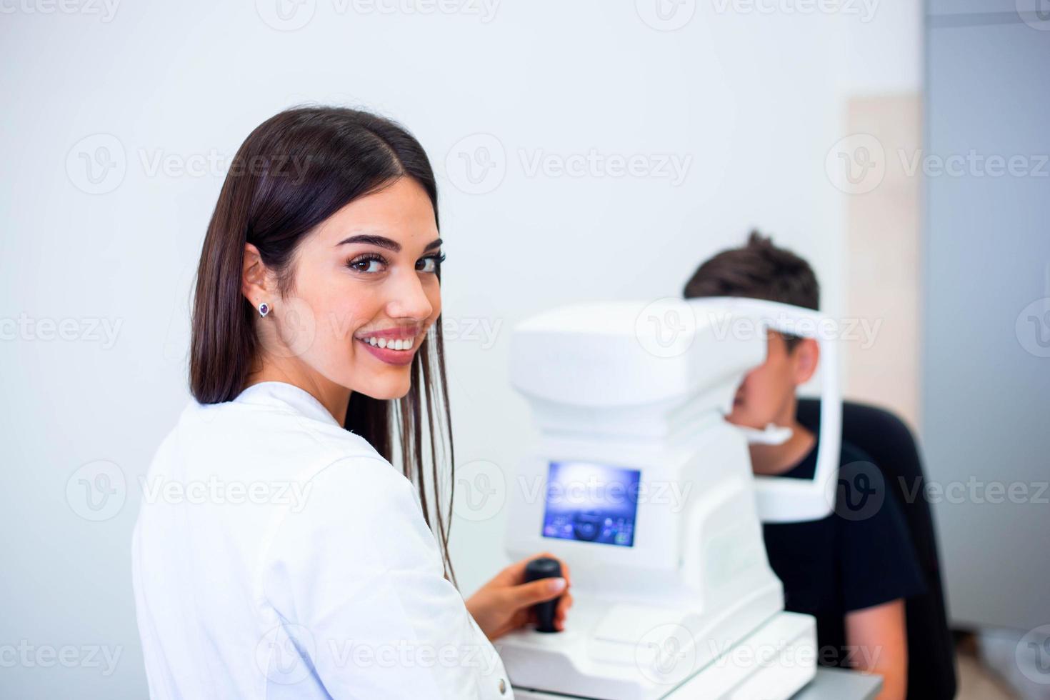 Female oculist using machine for checking eye sight in clinic. Little boy looking at equipment and doctor testing eye pupil in optical store. Concept of eye care and health. photo