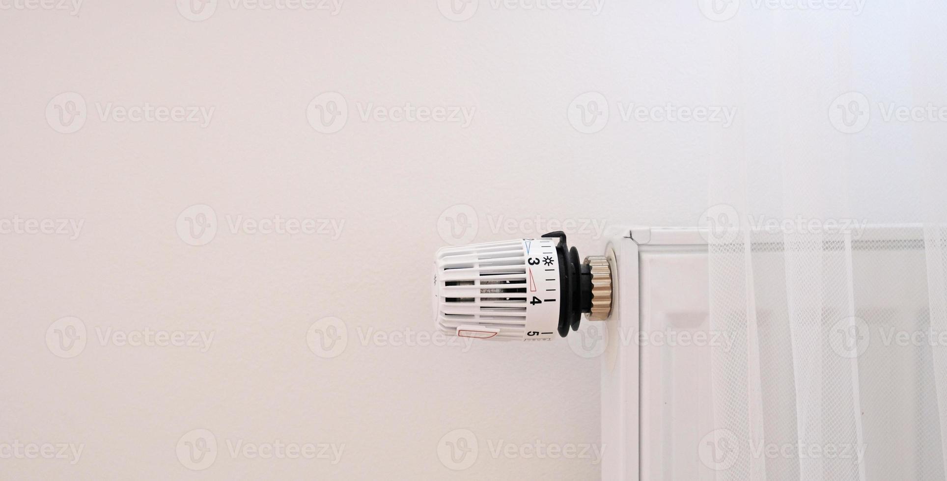 Banner with thermostat and battery temperature controller. Heating service cost concept, utility price increase. Temperature control valve. White heater on wall with curtain in modern apartment. photo