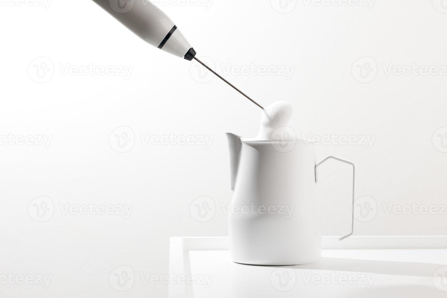 Making foamy milk with milk frother on a white table. photo