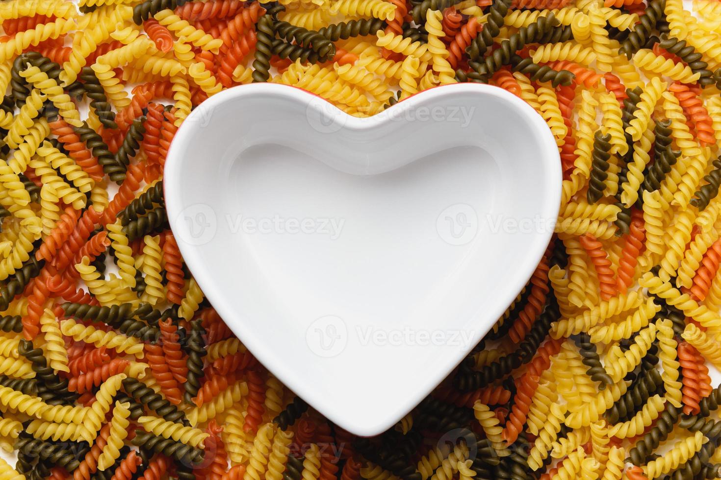 Raw pasta torti texture and white heart bowl. photo