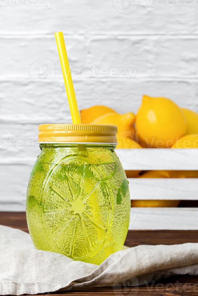 Water with mint in yellow glass, lemons in crate. photo