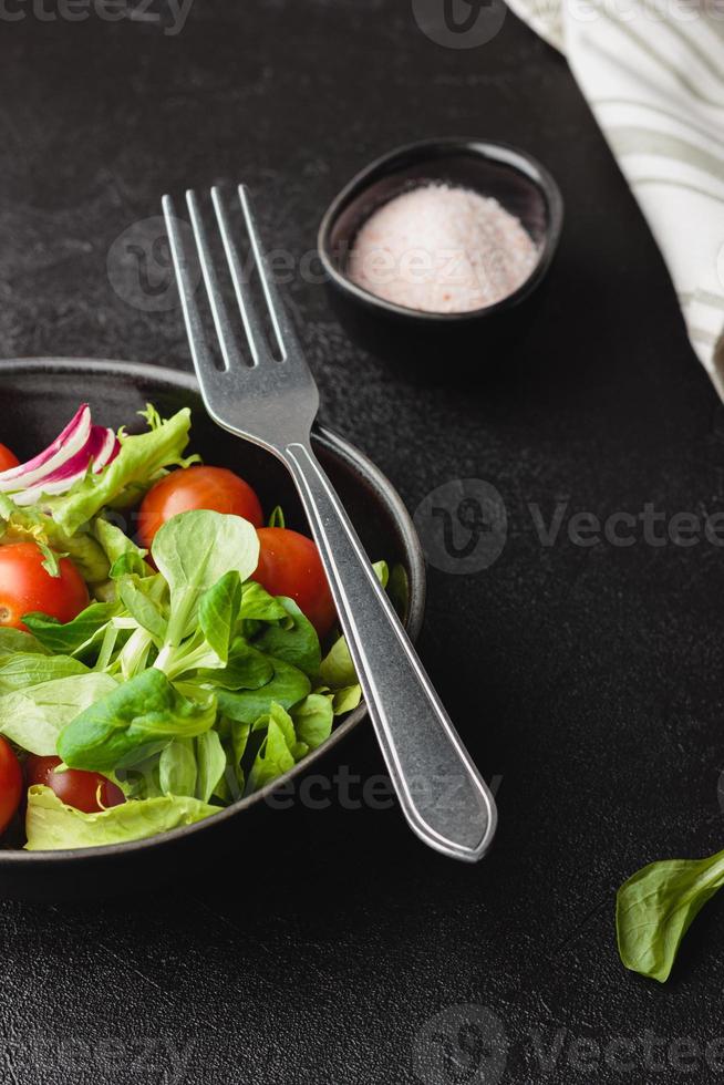 Green salad leaves with cherry tomatoes in bowl on black table. photo