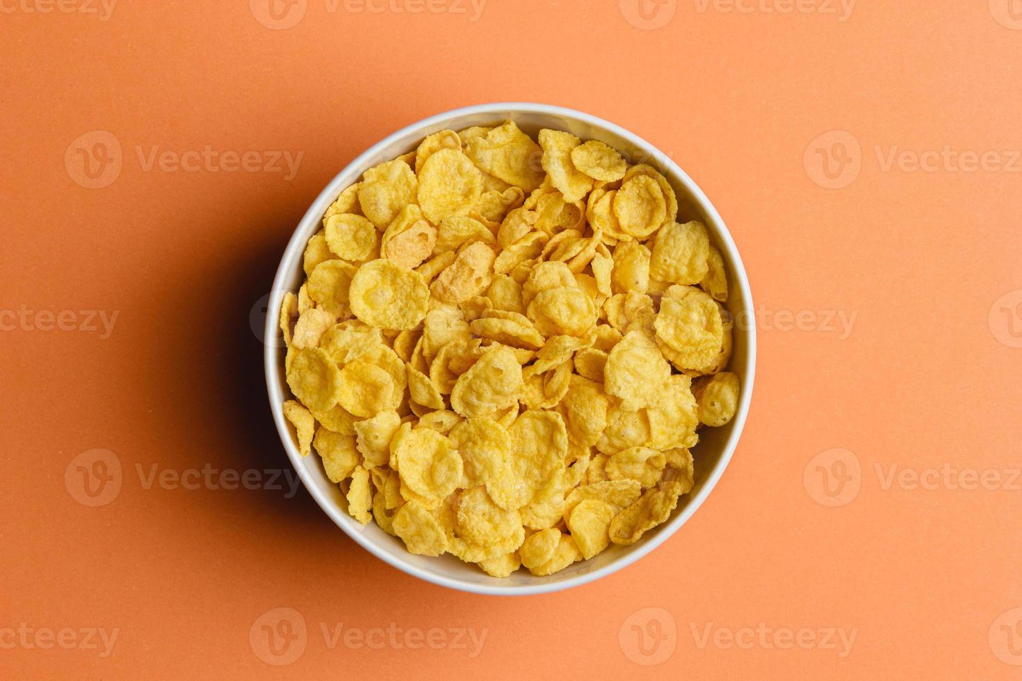 Corn flakes in white bowl on orange background. photo