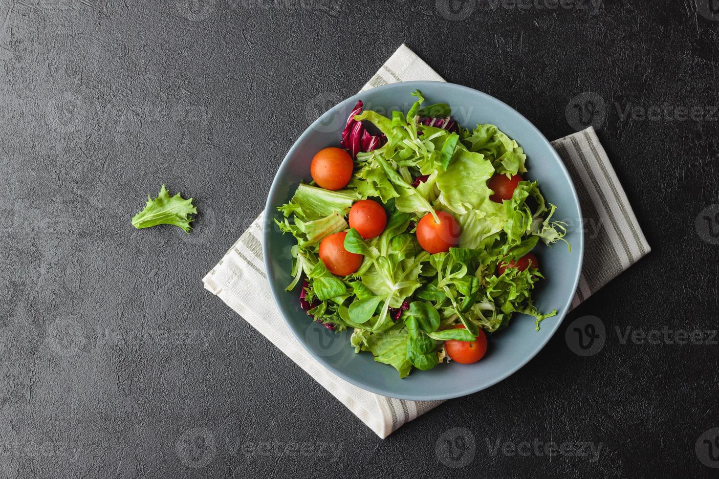 Green salad leaves with cherry tomatoes in bowl on black table. photo