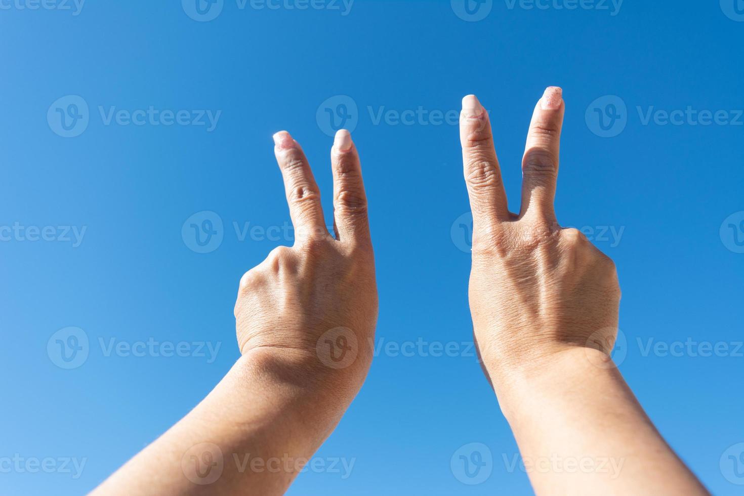 woman's hands showing sign of victorywoman's hands showing sign of victotia against blue sky background, photo