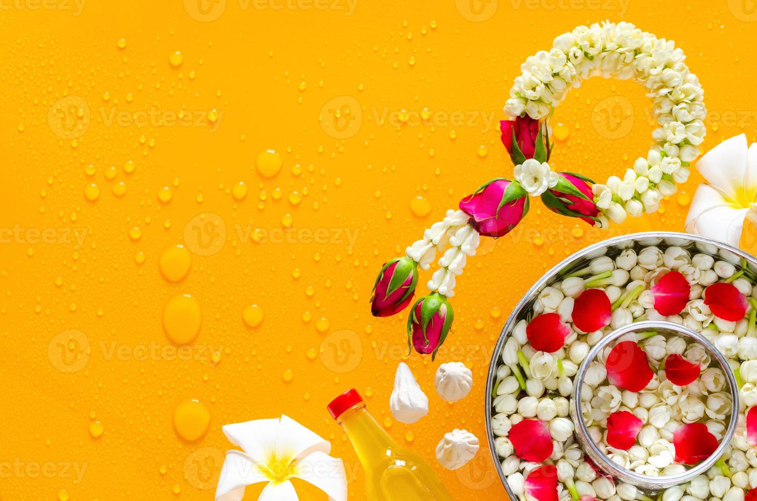 Songkran festival background with jasmine garland, flowers in water bowls, scented water and marly limestone put on clear mirror that have wet yellow background below. photo