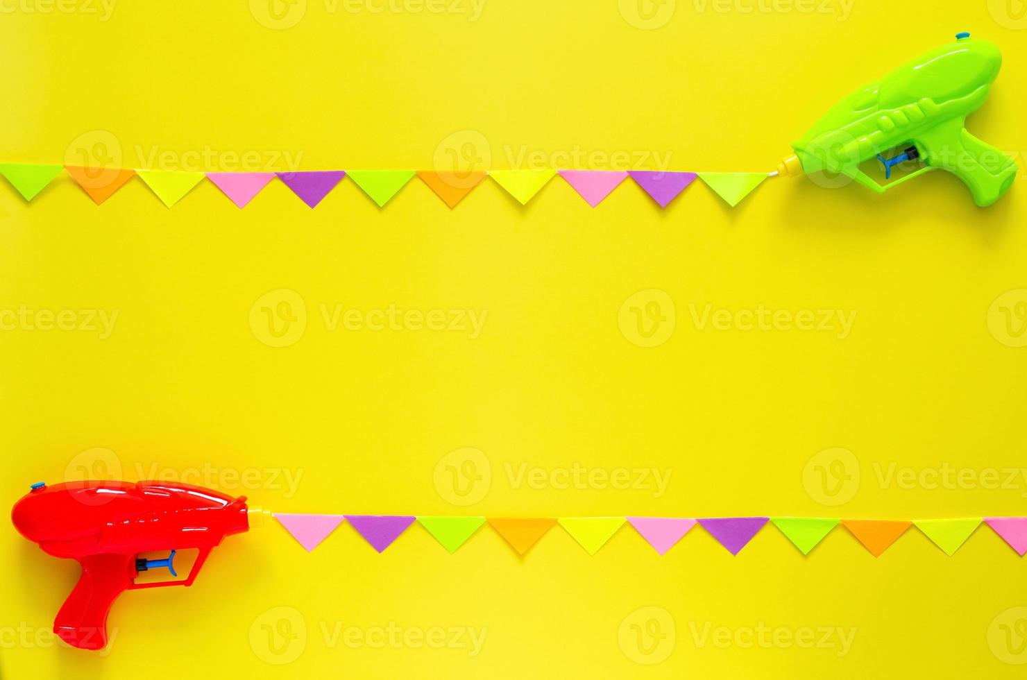 dos pistolas de agua se rocían con una colorida bandera de fiesta para la celebración del festival songkran con fondo de color amarillo. concepto mínimo de vacaciones. foto