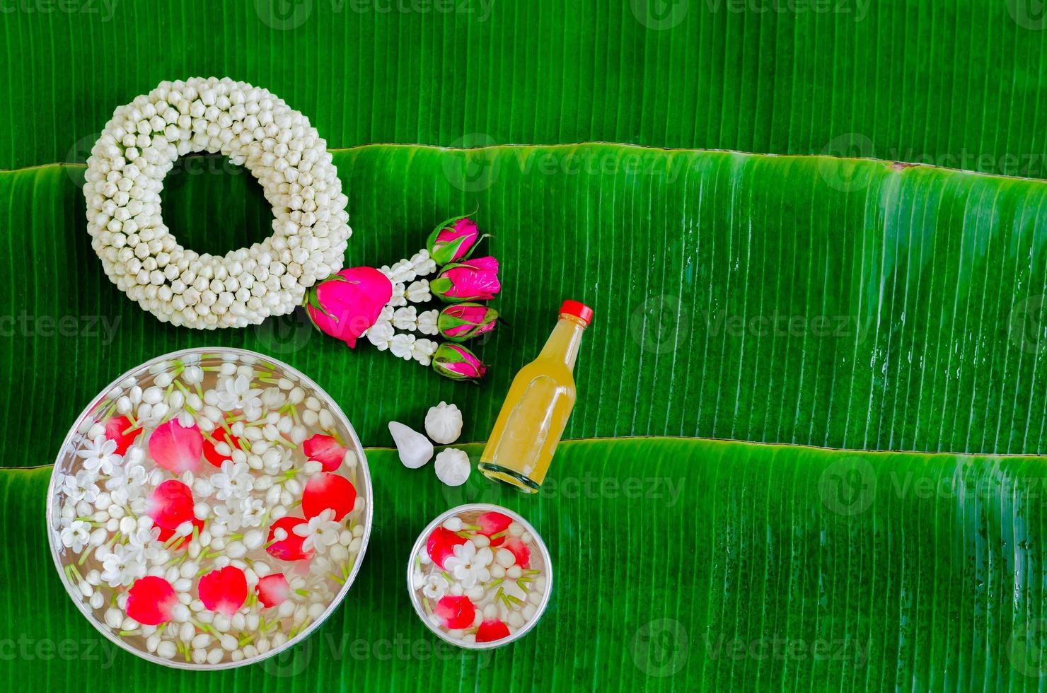 Songkran festival background with jasmine garland, flowers in water bowls, scented water and marly limestone for blessing on wet banana leaf background. photo